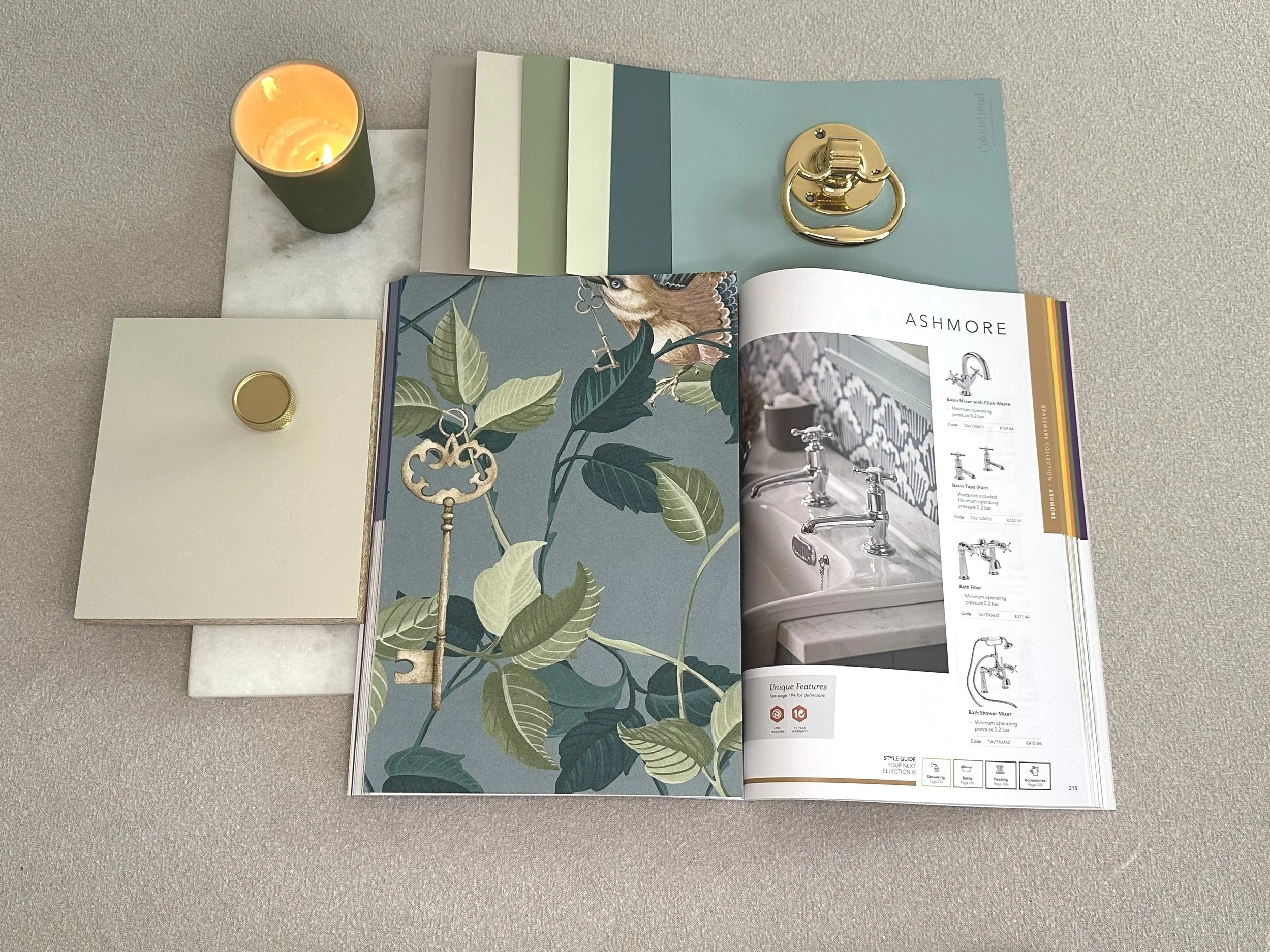 A selection of materials samples assembled by Bobby Lardner, interior designer,in teal and green tones for a Guest WC scheme - open catalog displaying bathroom fixtures, swatches of paint, wallpaper and brass samples, against a beige background.