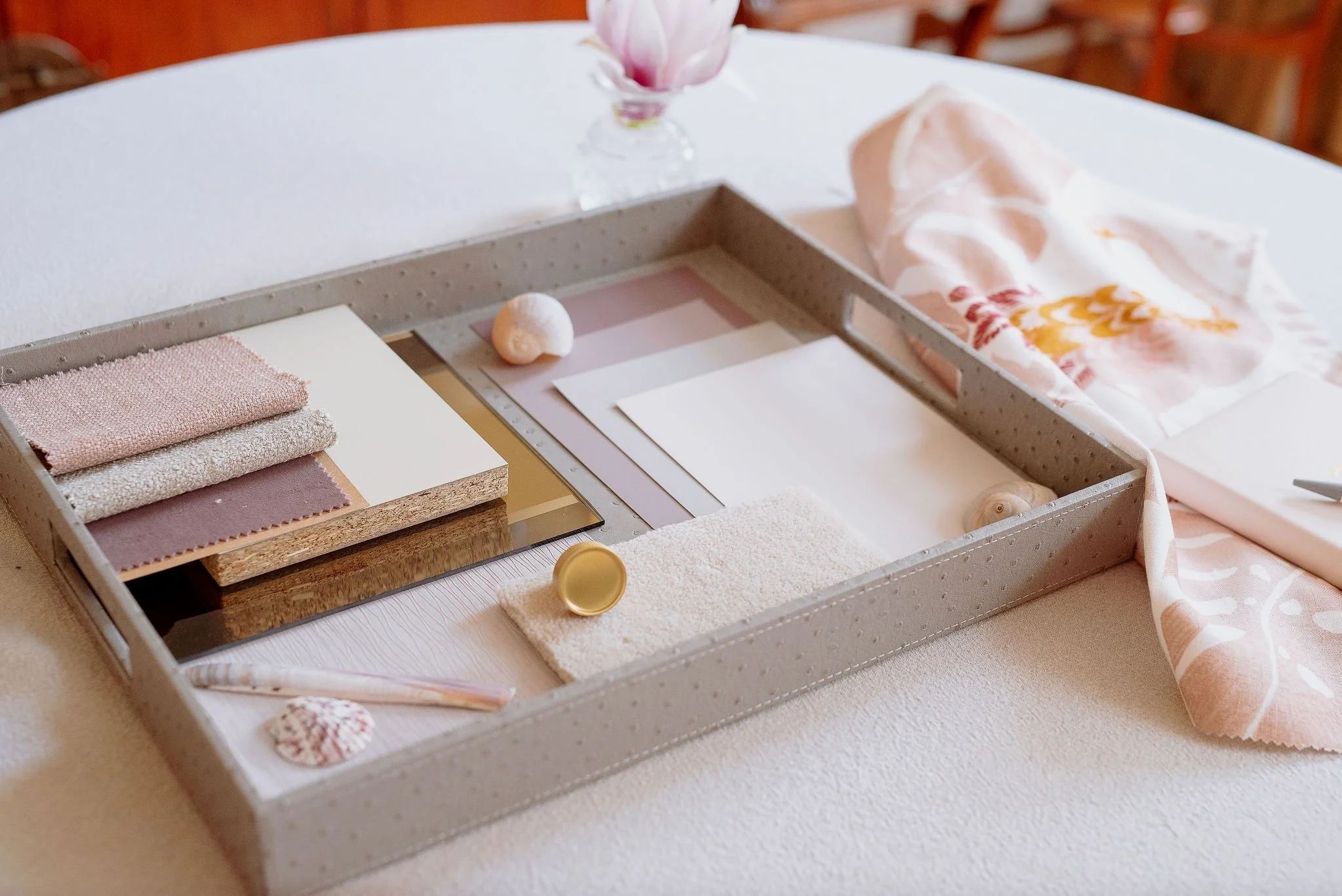 A selection of materials samples assembled by Bobby Lardner, interior designer, in soft pink tones for a luxurious bedroom scheme - fabric swatches, wallpapaper, marble, and supporting decorative items on a table.