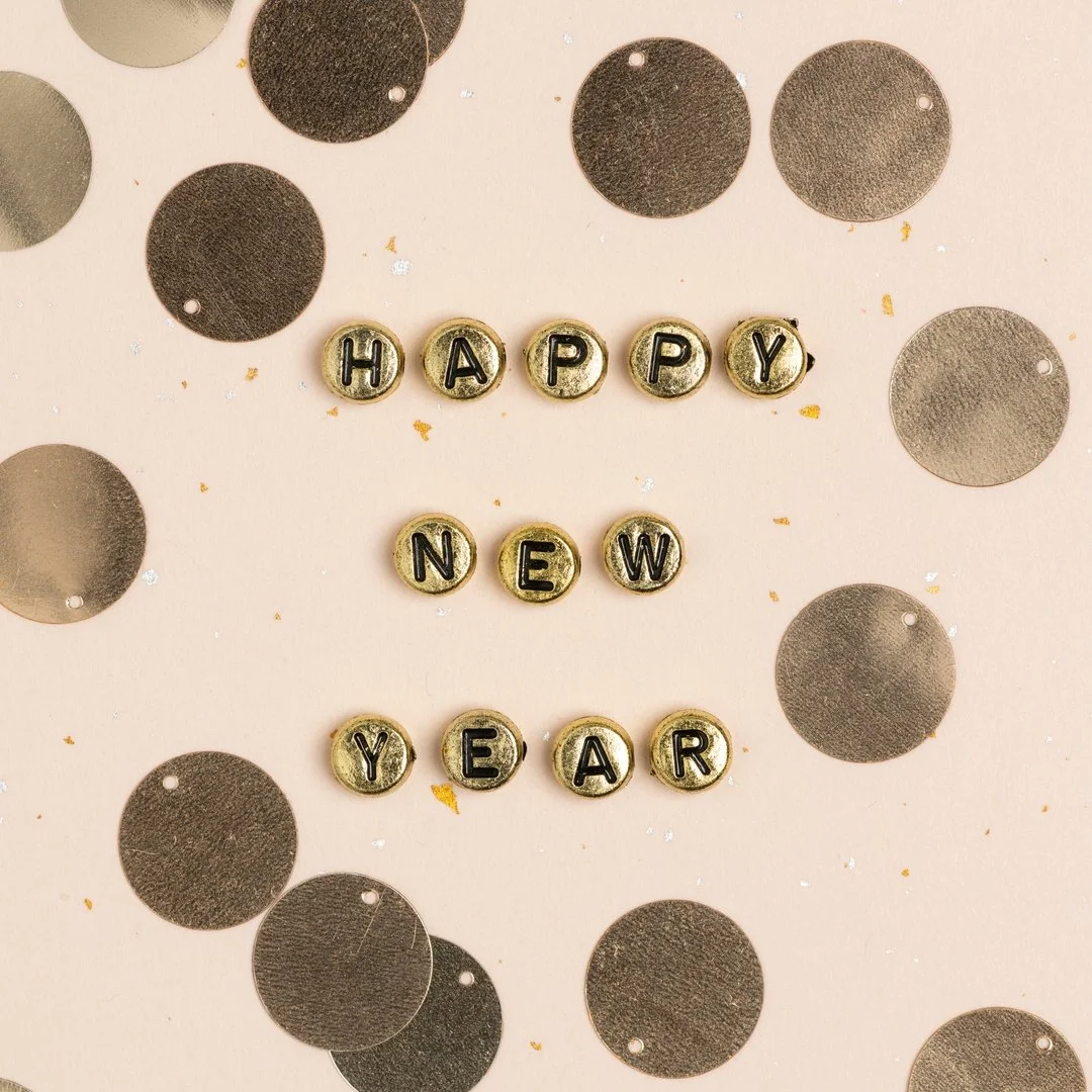 Letter beads spelling out "HAPPY NEW YEAR" on a pink background with black and silver confetti.