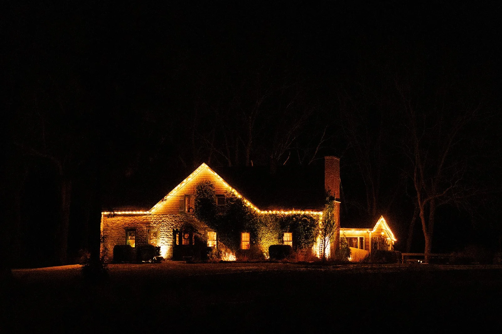 A house decorated with yellow string lights at night, with trees in the background and lights illuminating the exterior walls.