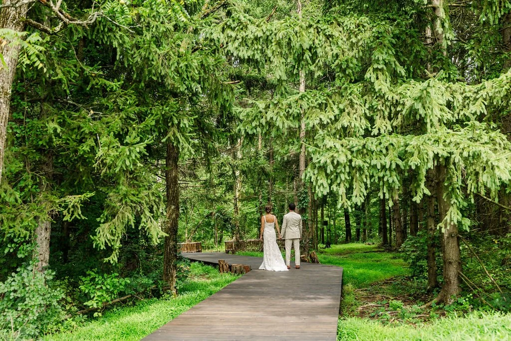 A bride and groom stroll into a majestic forest at Catskills wedding venue Black Walnut Farm