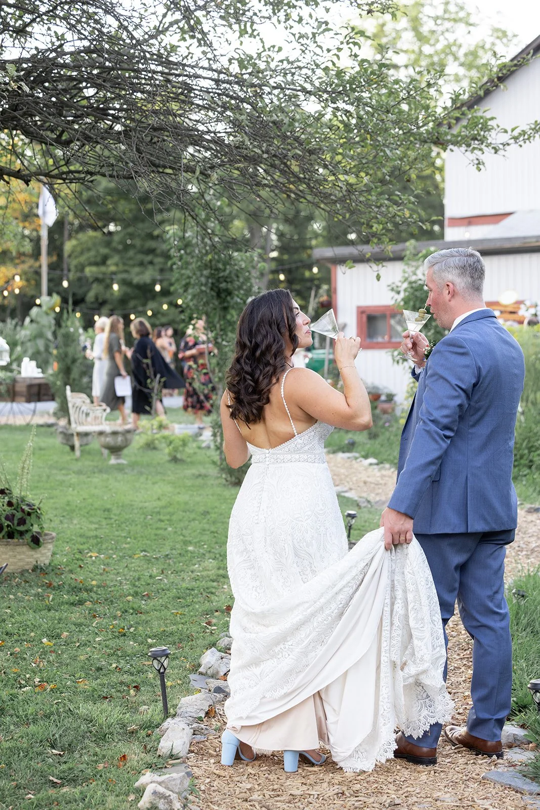 Bride and groom drinking cocktails at an outdoor wedding reception, with guests mingling in the background.