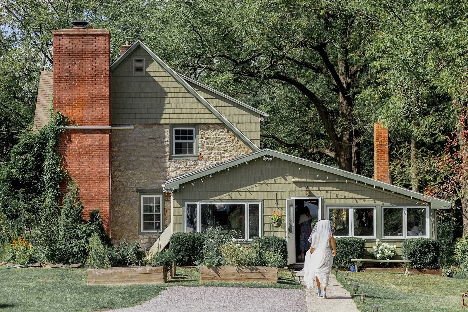 A bride walks through a garden to the ivy covered farmhouse at Black Walnut Farm
