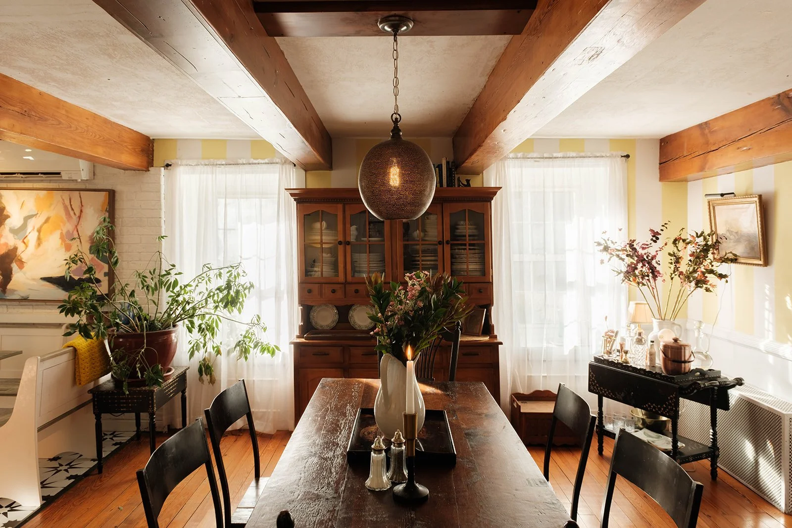 An sunny dining room with antique beams, an antique dining table, a chandelier and a festive bar cart