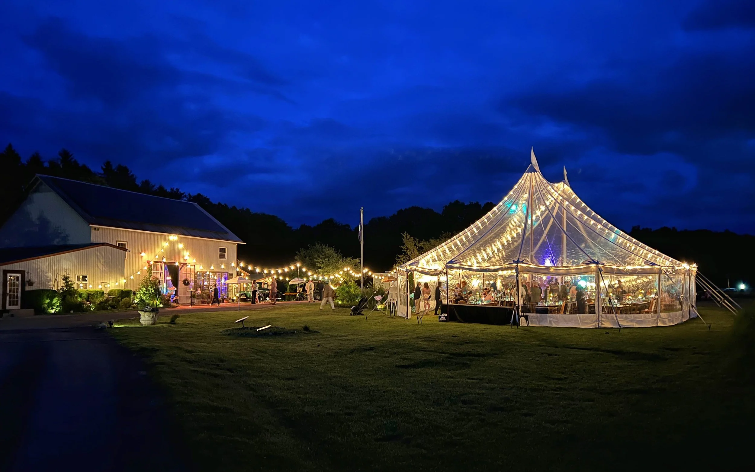 A festive view of the barn at Black Walnut Farm at night, illuminated with a clear tent on the lawn
