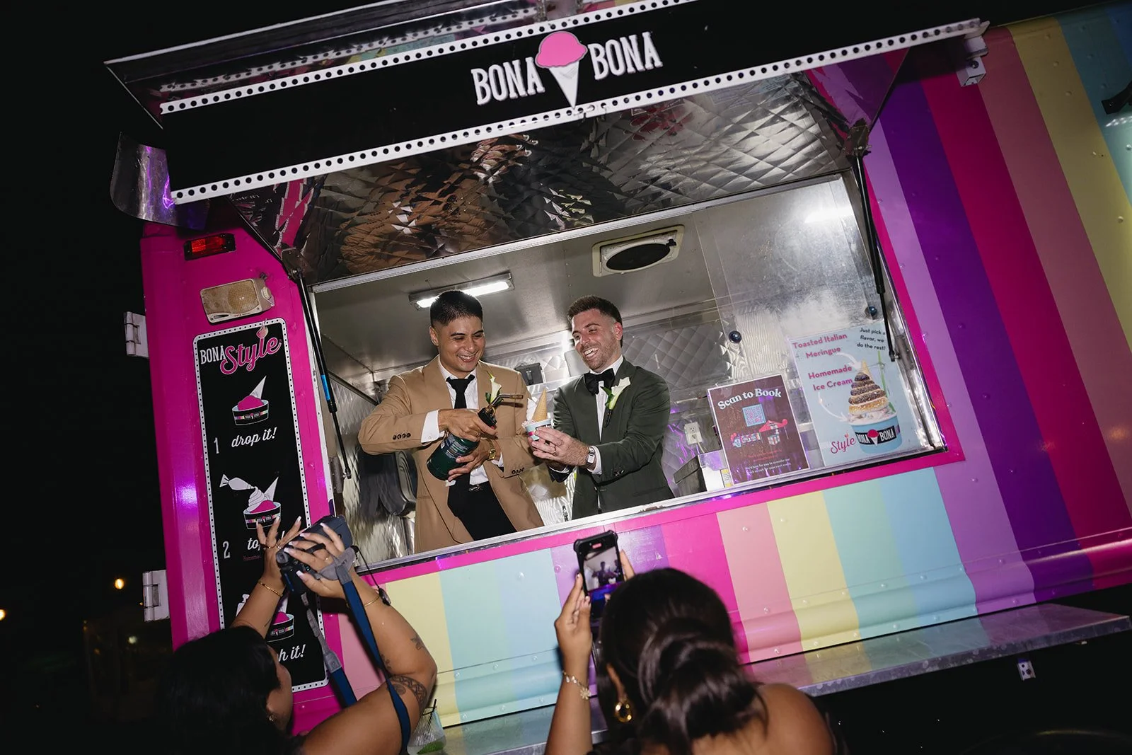 Two grooms laugh and serve their wedding guests ice cream from an ice cream truck at their wedding