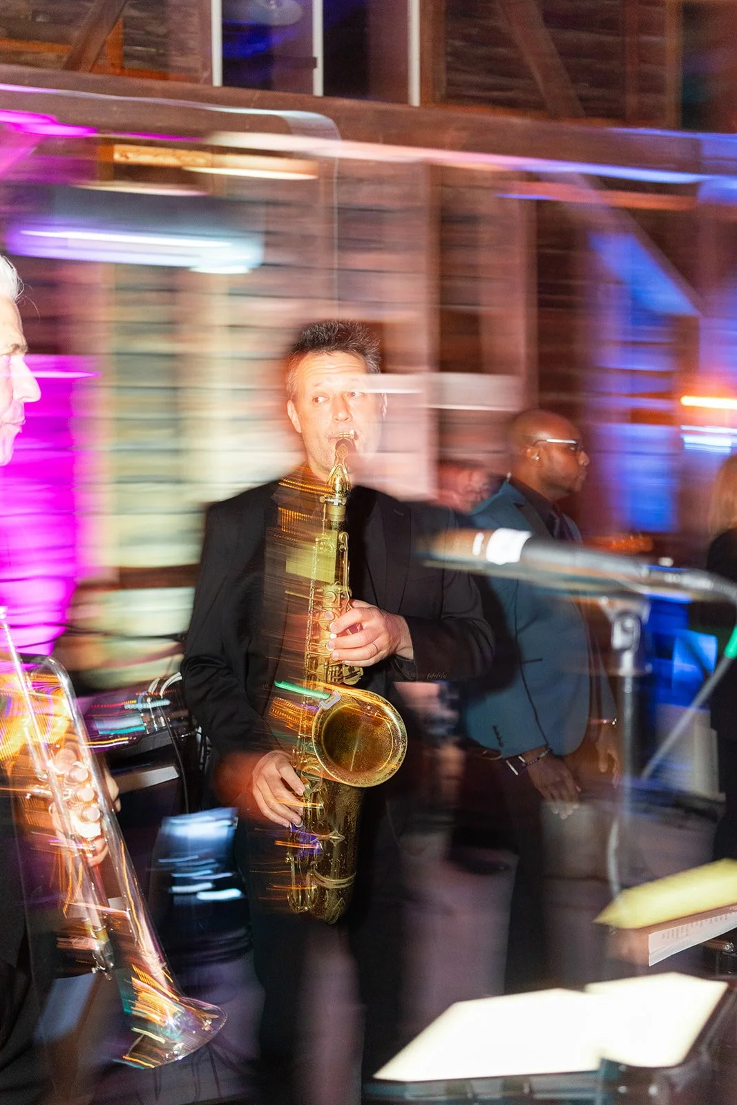 Musicians performing at a lively event with colorful lighting, including a man playing the saxophone.