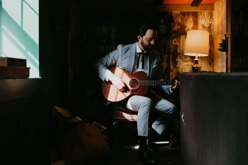 A man in a blue suit playing a guitar in a moody living room