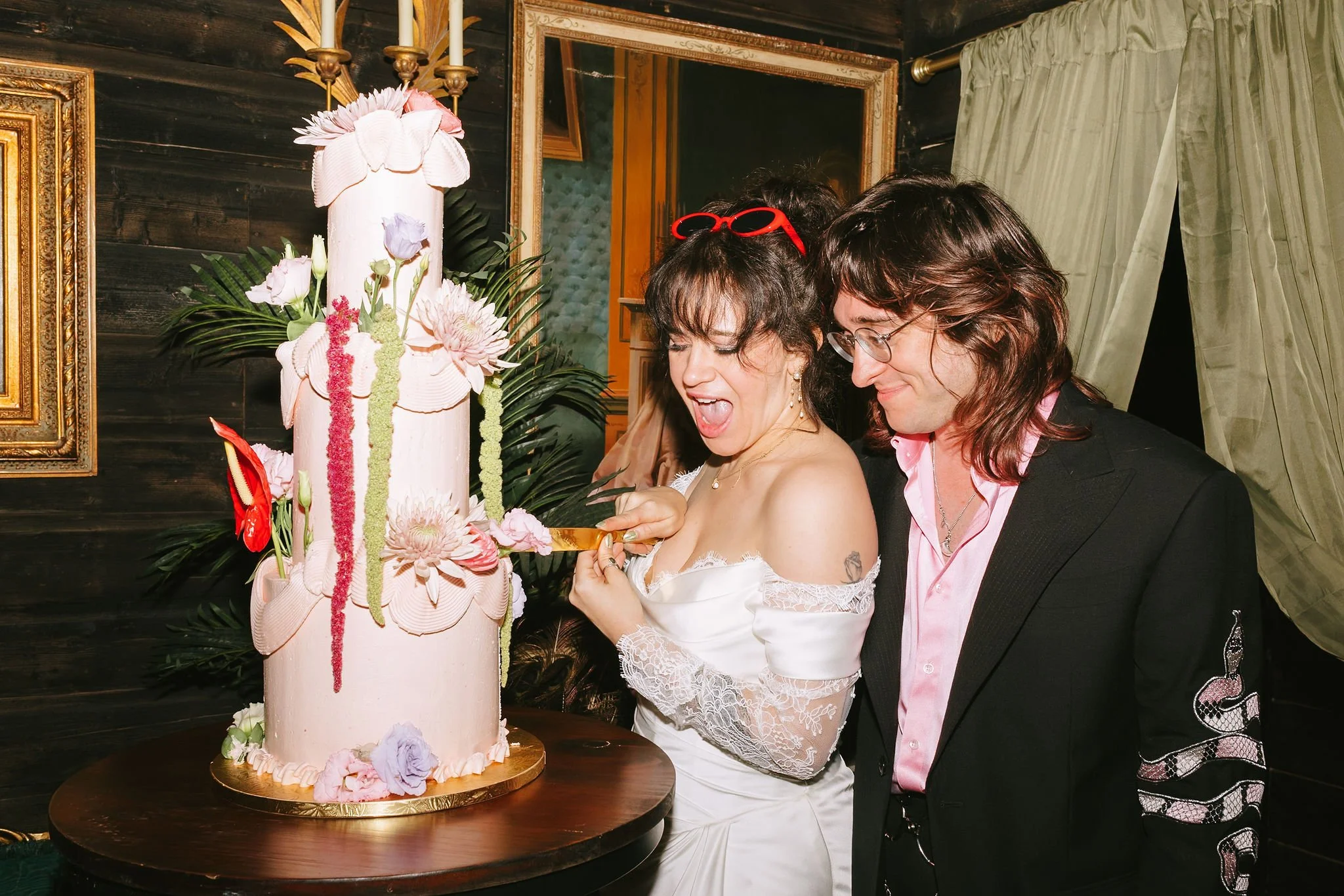 A bride and groom slice into an enormous pink wedding cake in the barn at Black Walnut Farm