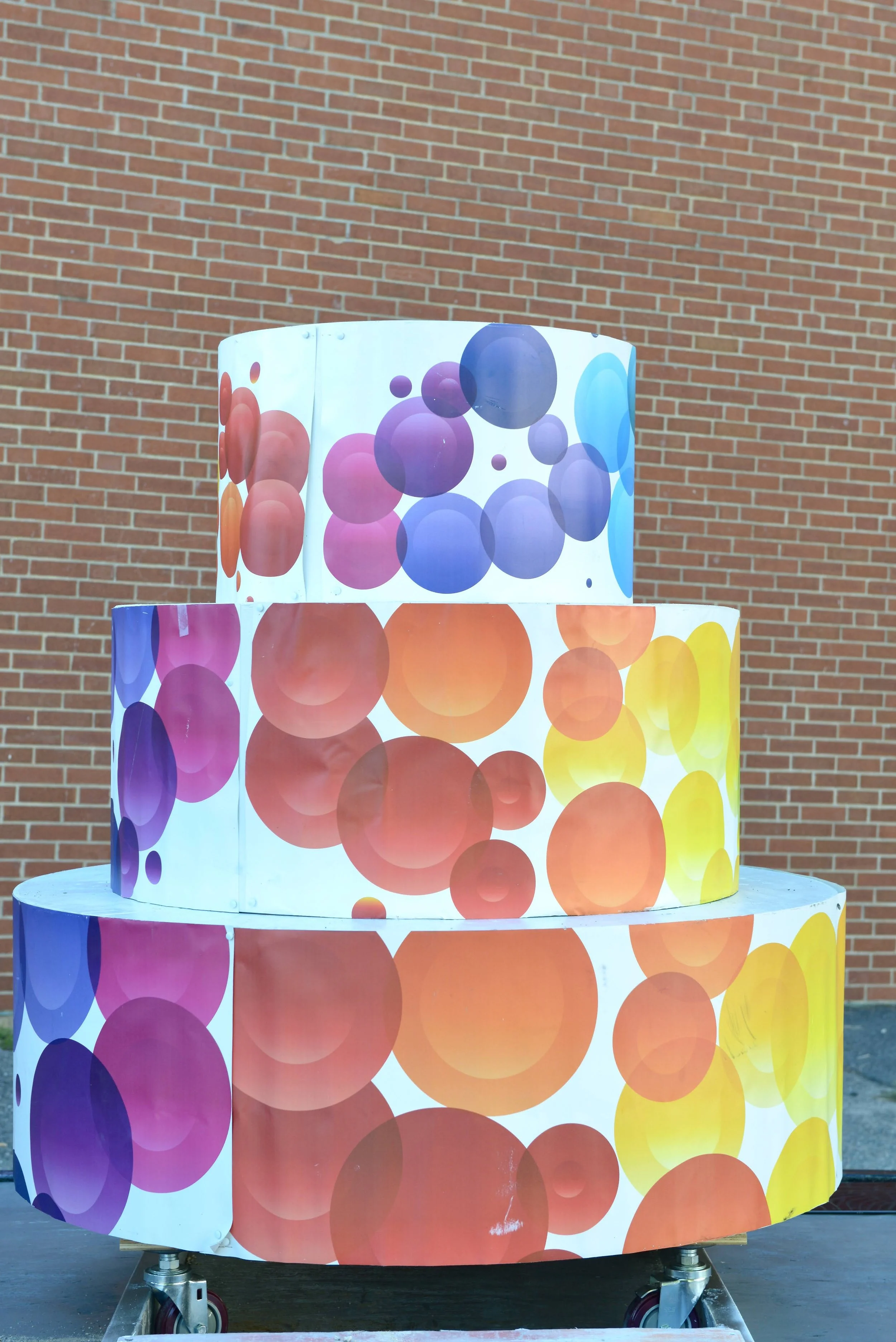 Colorful three-tiered display decorated with large, overlapping circles in various shades of purple, blue, orange, and yellow, set against a brick wall background.