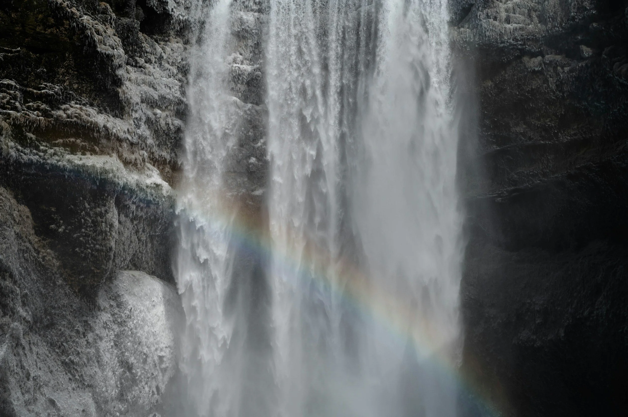 A waterfall cascading down rocky cliffs with a visible rainbow in the mist.