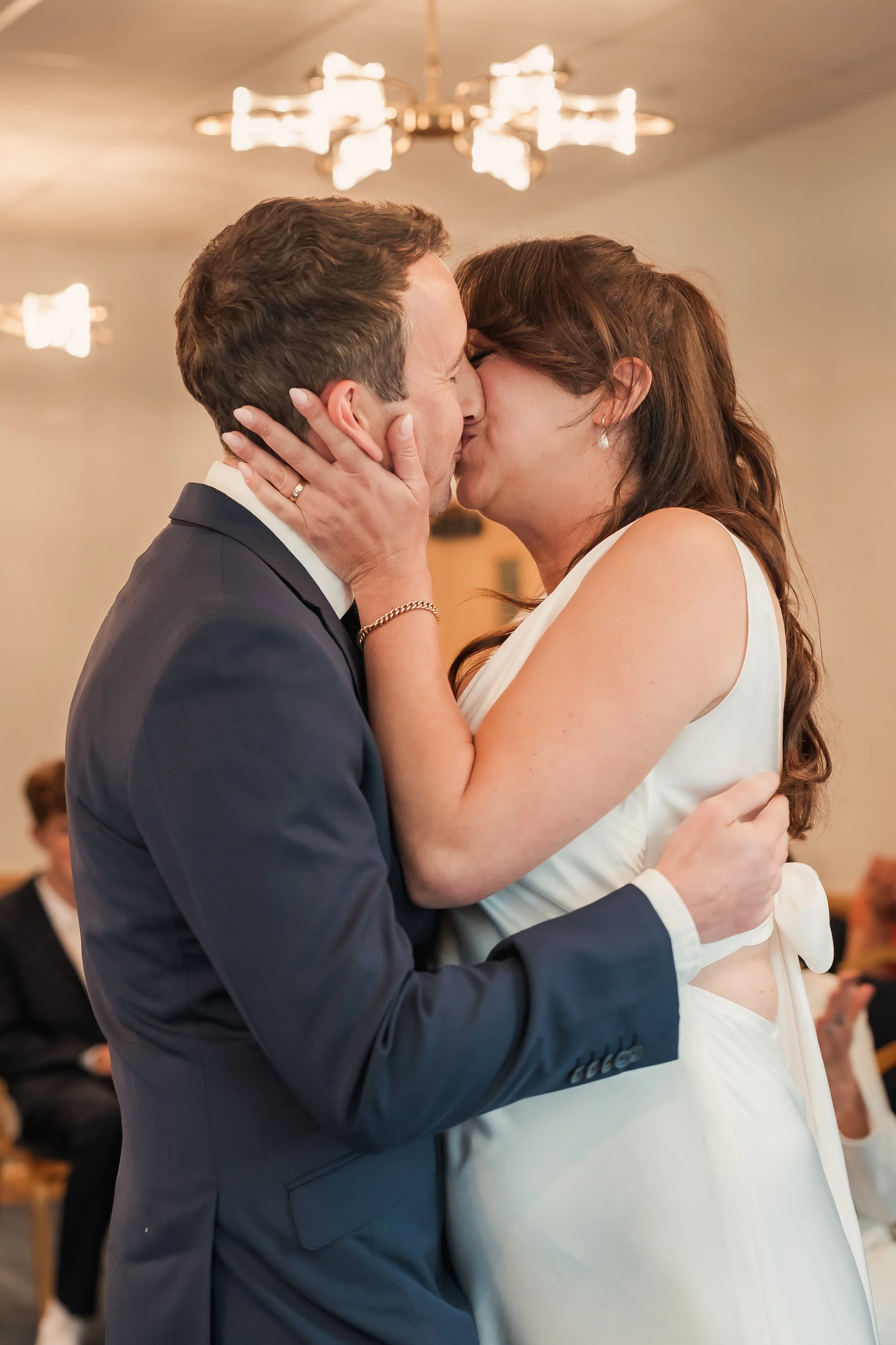 A couple passionately kissing during their wedding ceremony. The groom in a dark suit and the bride in a white dress are holding each other closely.