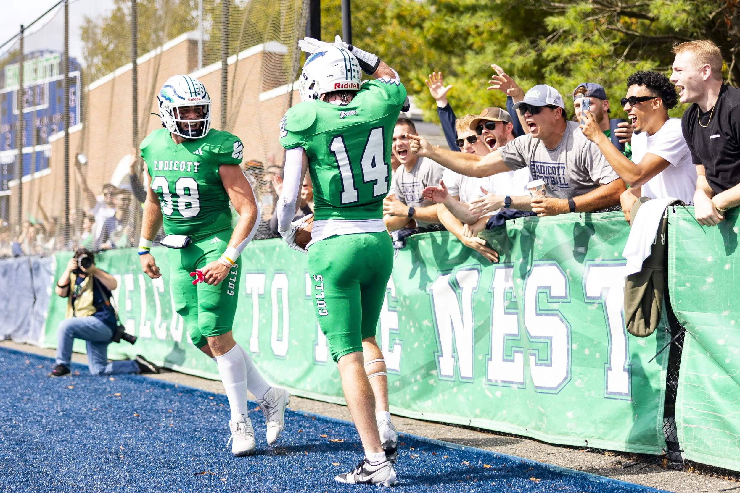 Football players in green uniforms celebrating after scoring, with fans reaching out from the sideline.