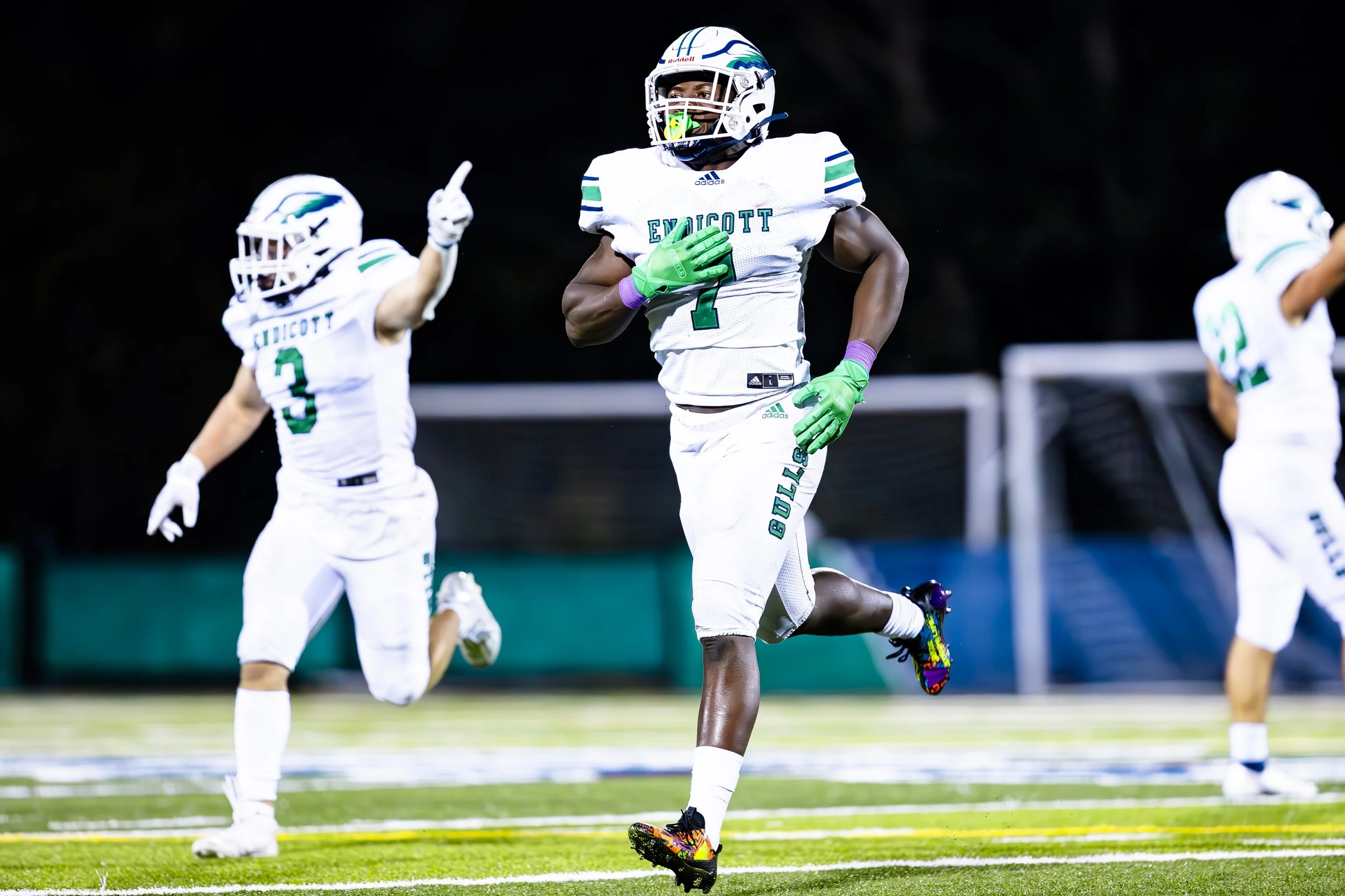 American football players in white uniforms with green accents, running on a football field at night, celebrating during a game.