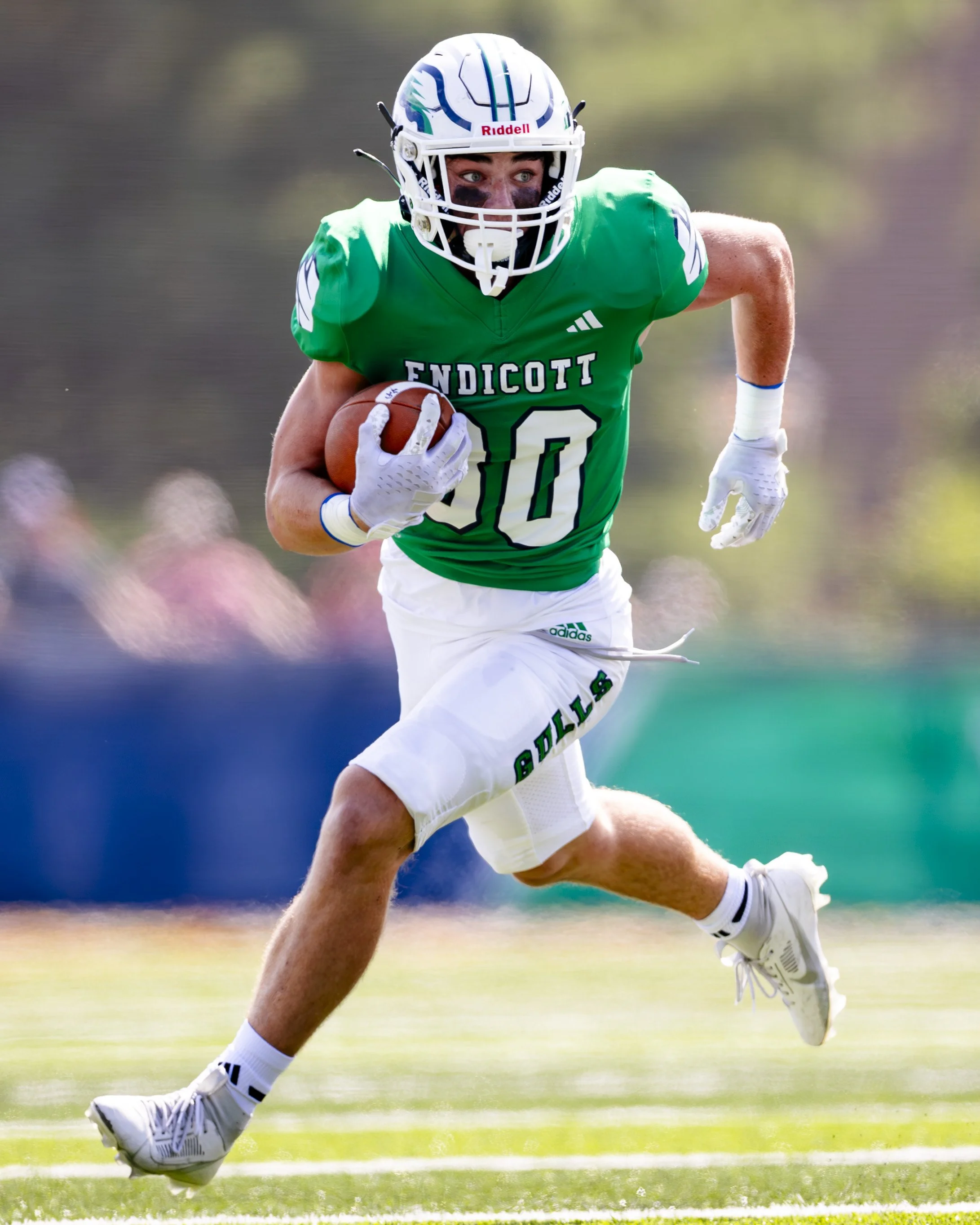 A football player wearing a green jersey with number 10, running on the field while holding a football in his right arm.