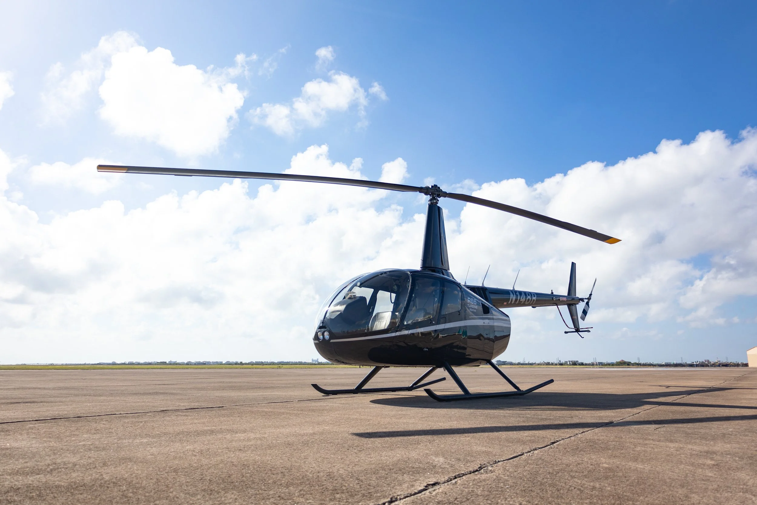 A black helicopter on an airfield with a partly cloudy sky in the background.