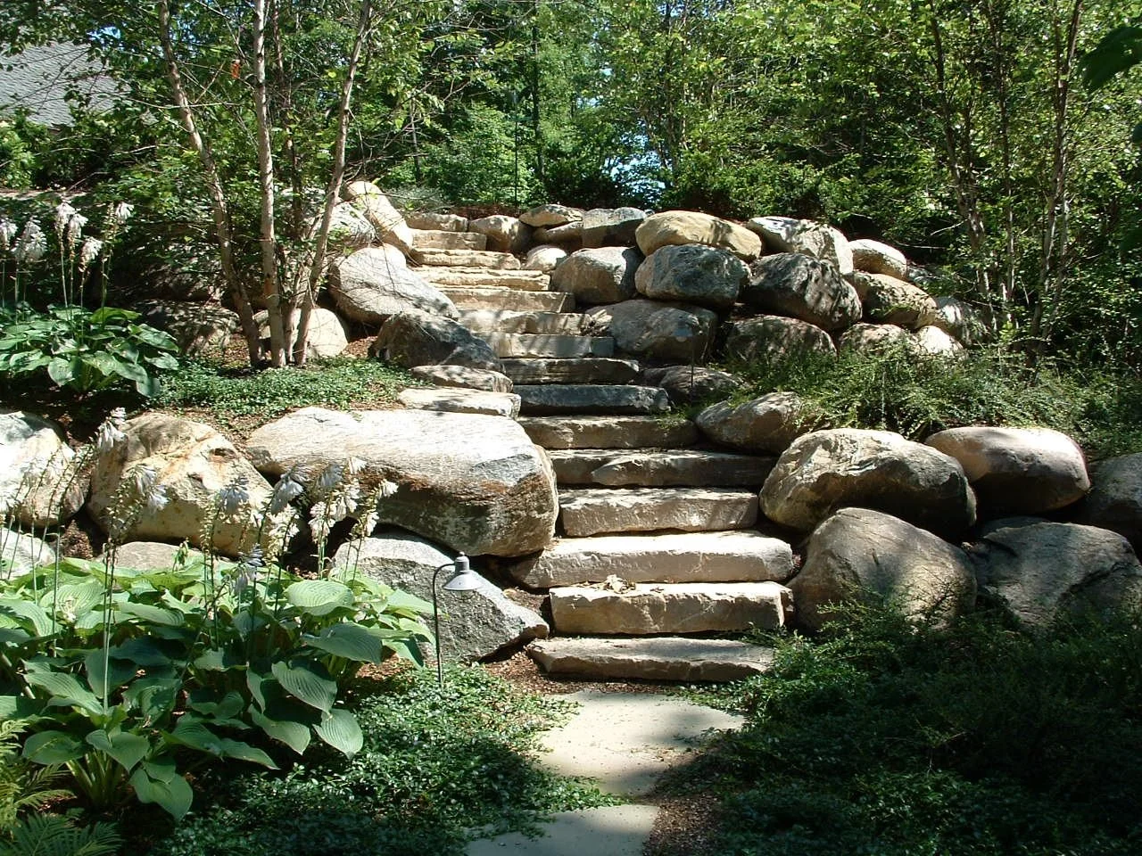 Upcott's Landscaping and Design. Stone staircase surrounded by trees and bushes in a garden setting.