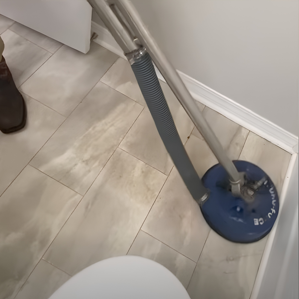 A close-up of a wet/dry vacuum cleaner on a marble tile floor near a white wall and baseboard, with part of a person's foot in a dark shoe visible on the left.