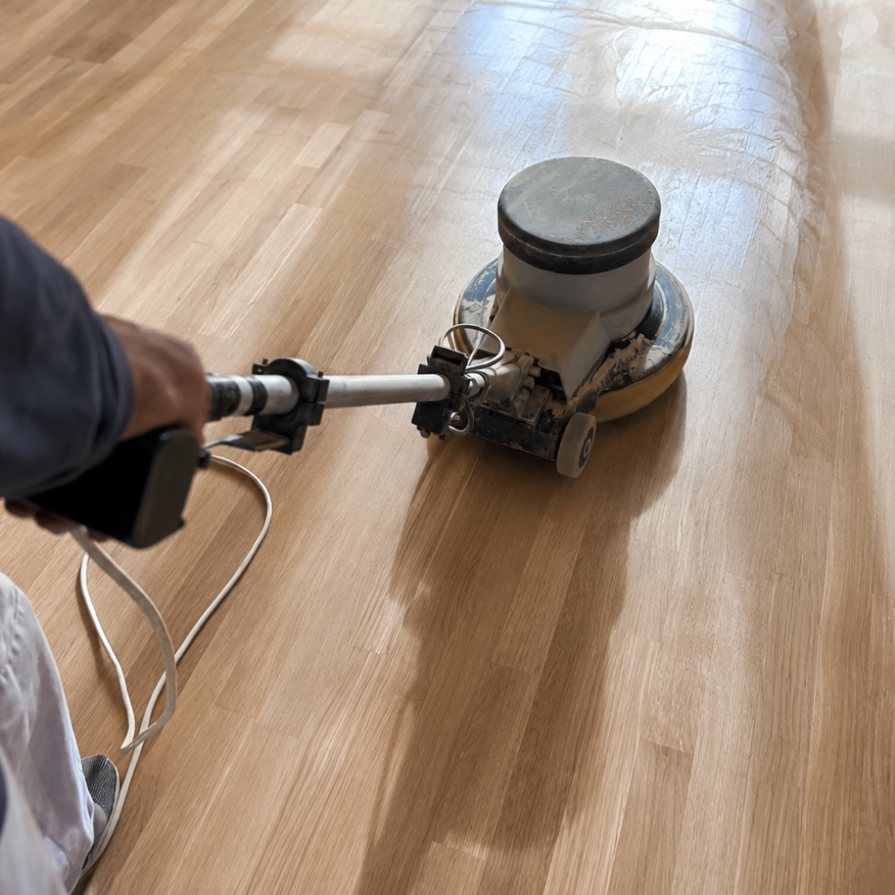 A person using a floor sander to sand a wooden floor.