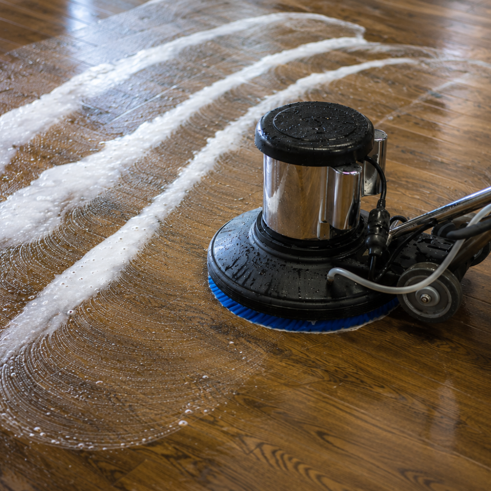 A floor polishing machine cleaning a wooden floor, creating wet streaks and soap suds.