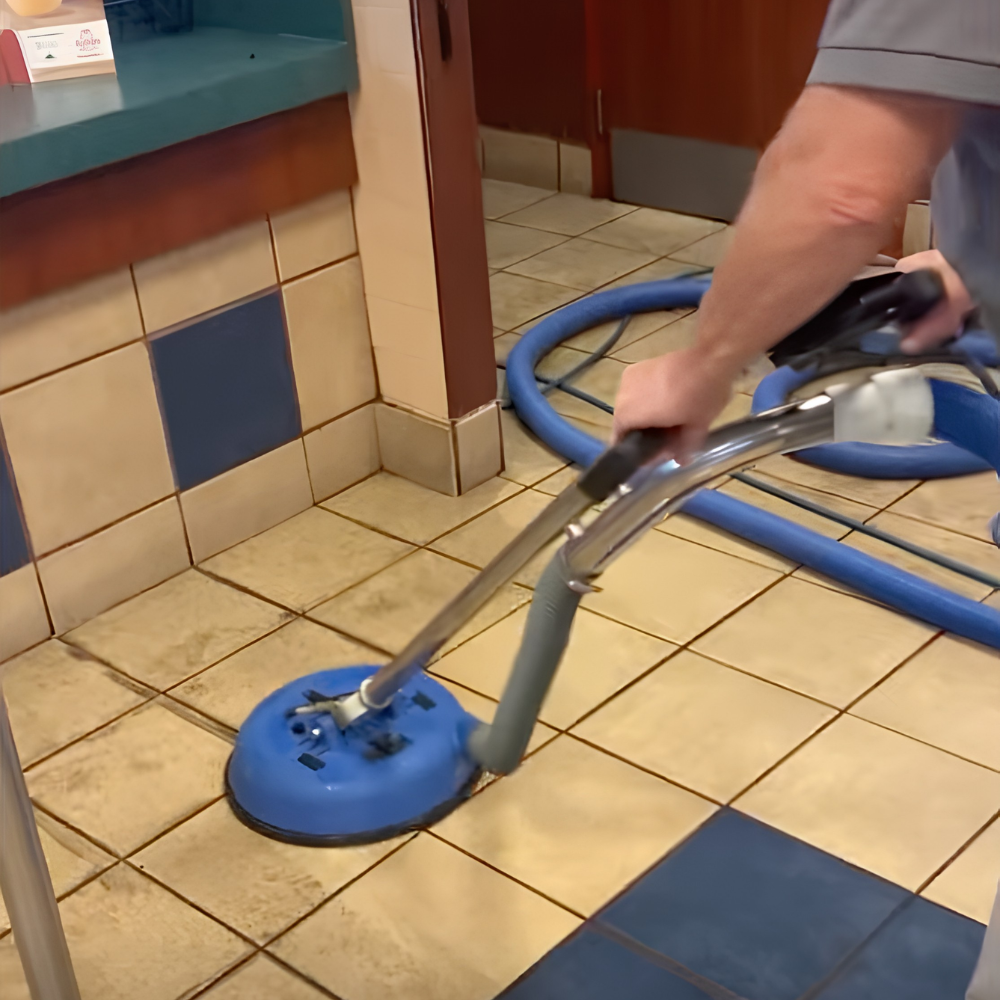 A person using a floor buffer or polisher on a tiled floor in a commercial kitchen or restaurant.