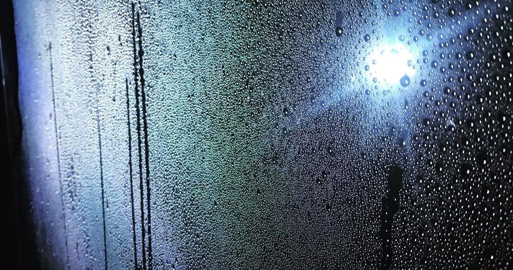  ID:A close up photo of the windscreen which is wet as if it has been raining, a single light shines through the darkness as if at night. 