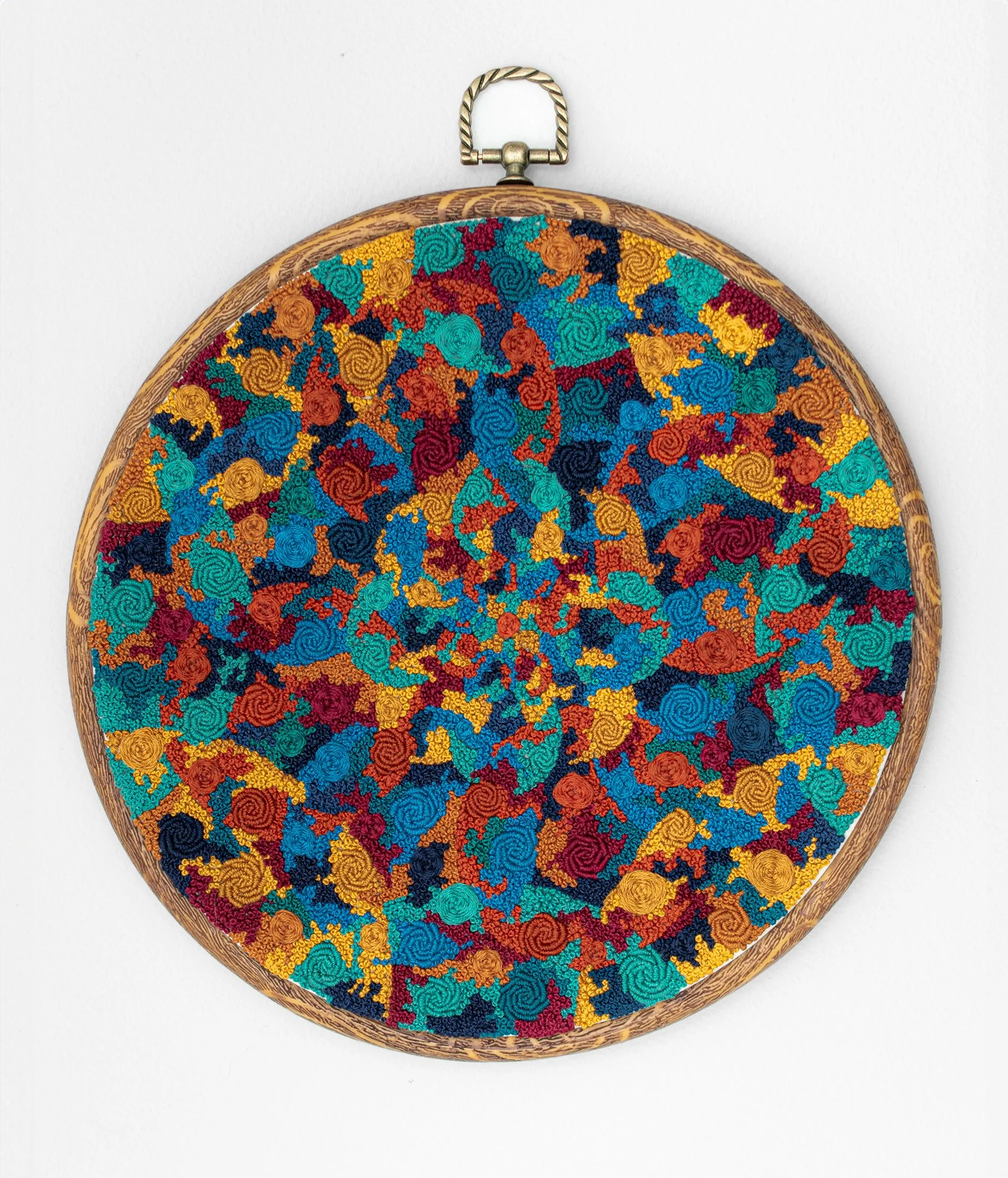Multi-colored embroidery framed in a hoop, with bullion roses, pinwheel flowers, and french knots covering the fabric