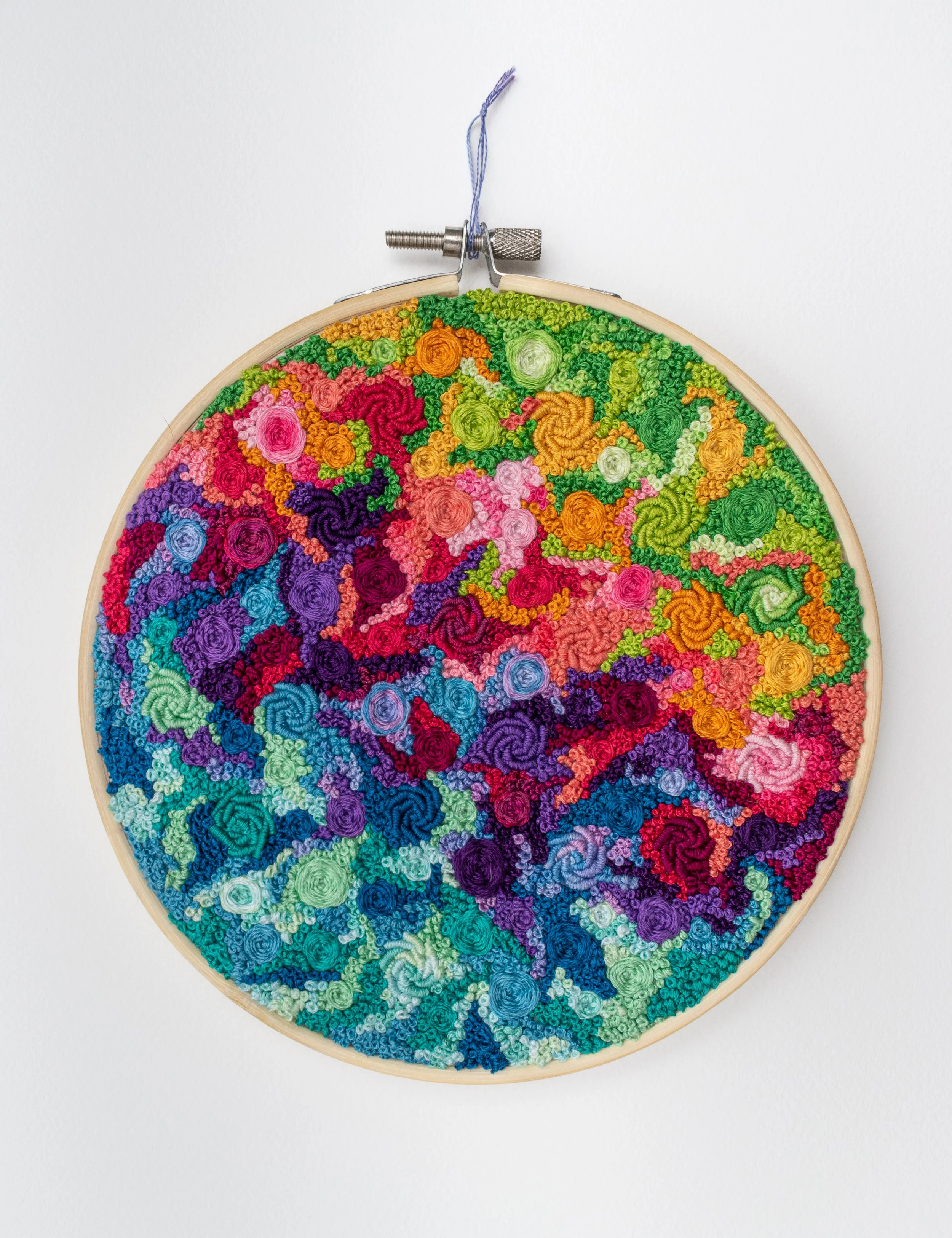 Colorful rainbow hand embroidery in a hoop, with bullion roses, pinwheel flowers, and french knots covering the fabric