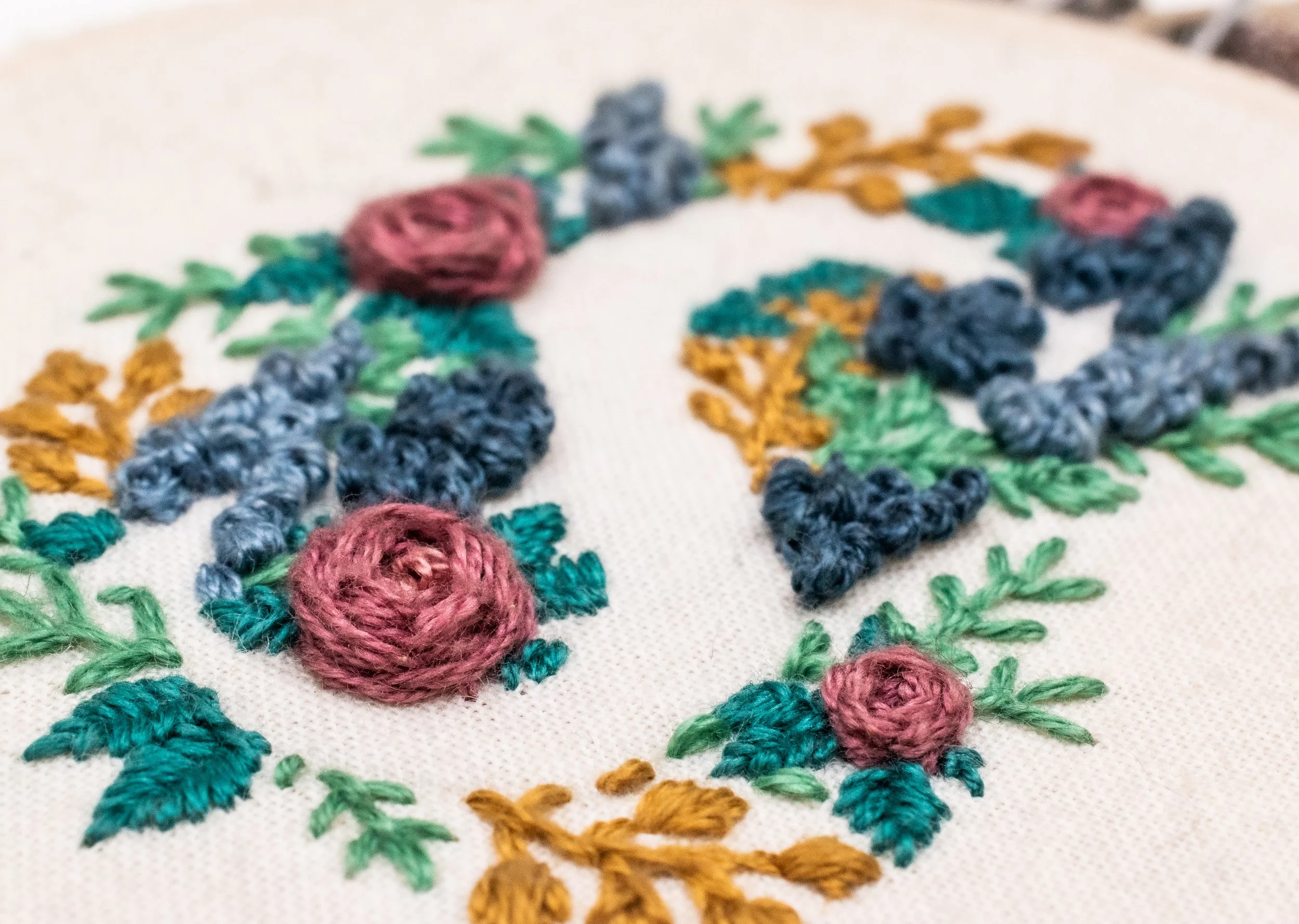 Close-up of hand embroidery depicting an S in negative space surrounded by flowers