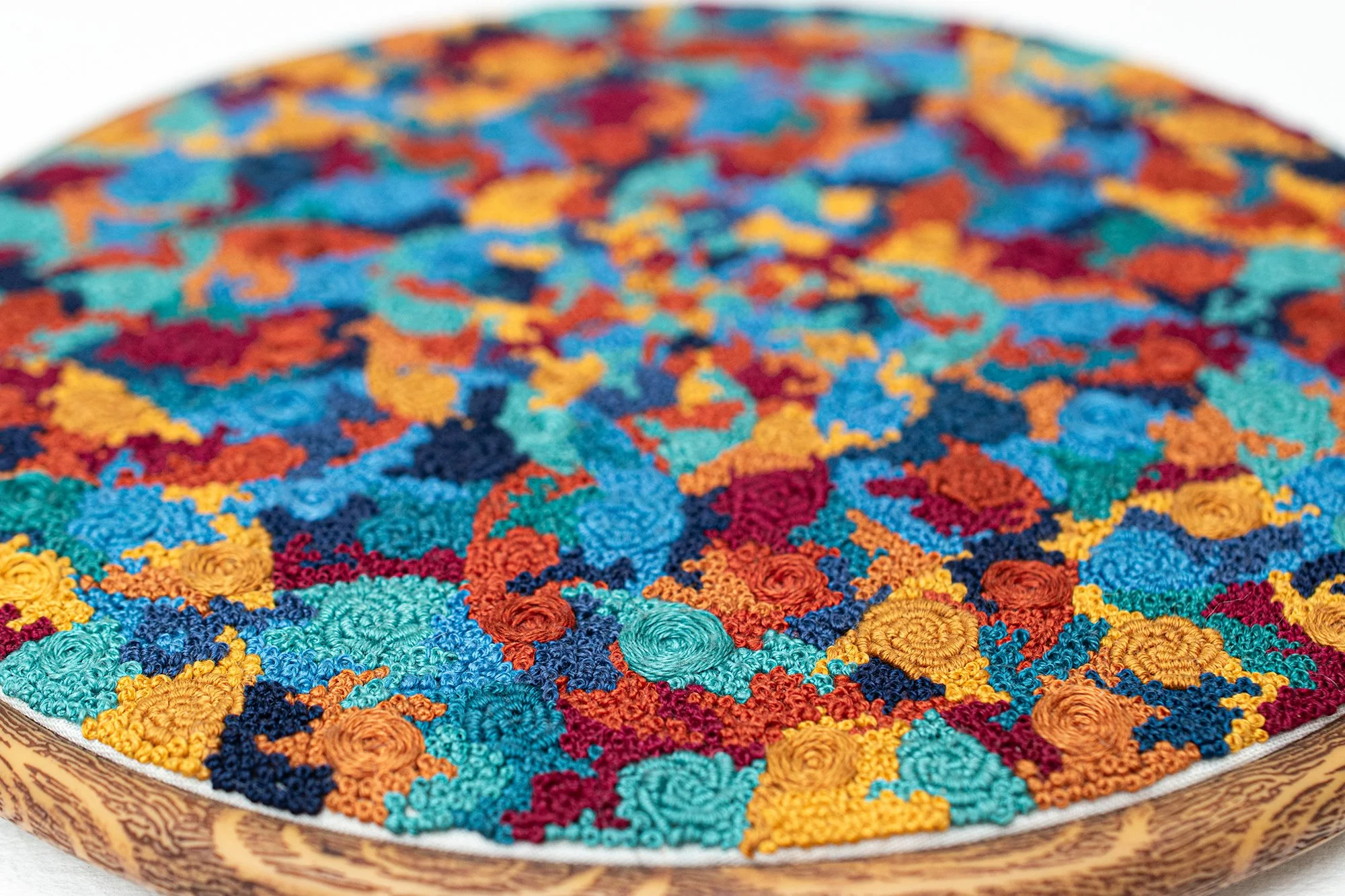 Close-up of colorful embroidery in a hoop, with bullion roses, pinwheel flowers, and french knots covering the fabric