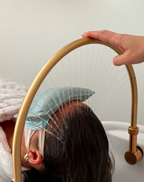 Person receiving a feather therapy treatment with a gold frame and white feathers, lying down with a towel, face covered with a sleep mask, in a wellness setting.