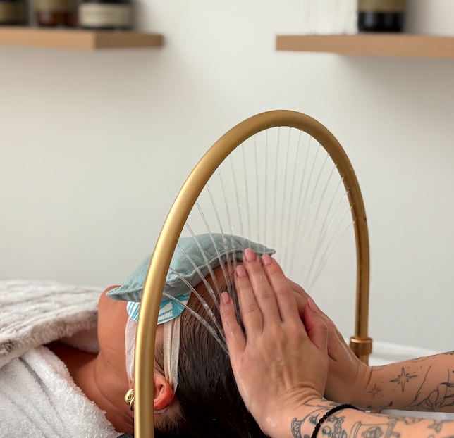Person receiving a facial massage with their face resting on a pillow, with a gold frame structure in the background.