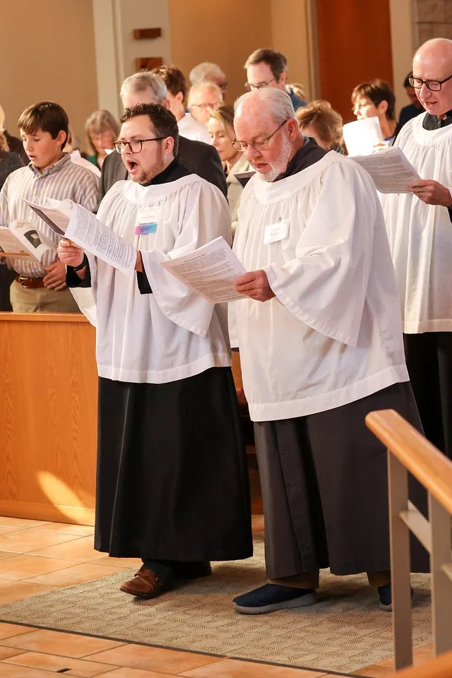 People dressed in white robes and black cassocks singing in a church during a religious service.