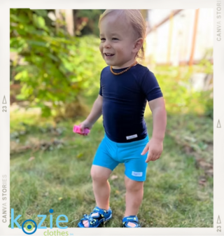A toddler standing outside in light blue Kozie sensory friendly compression shorts and a navy top