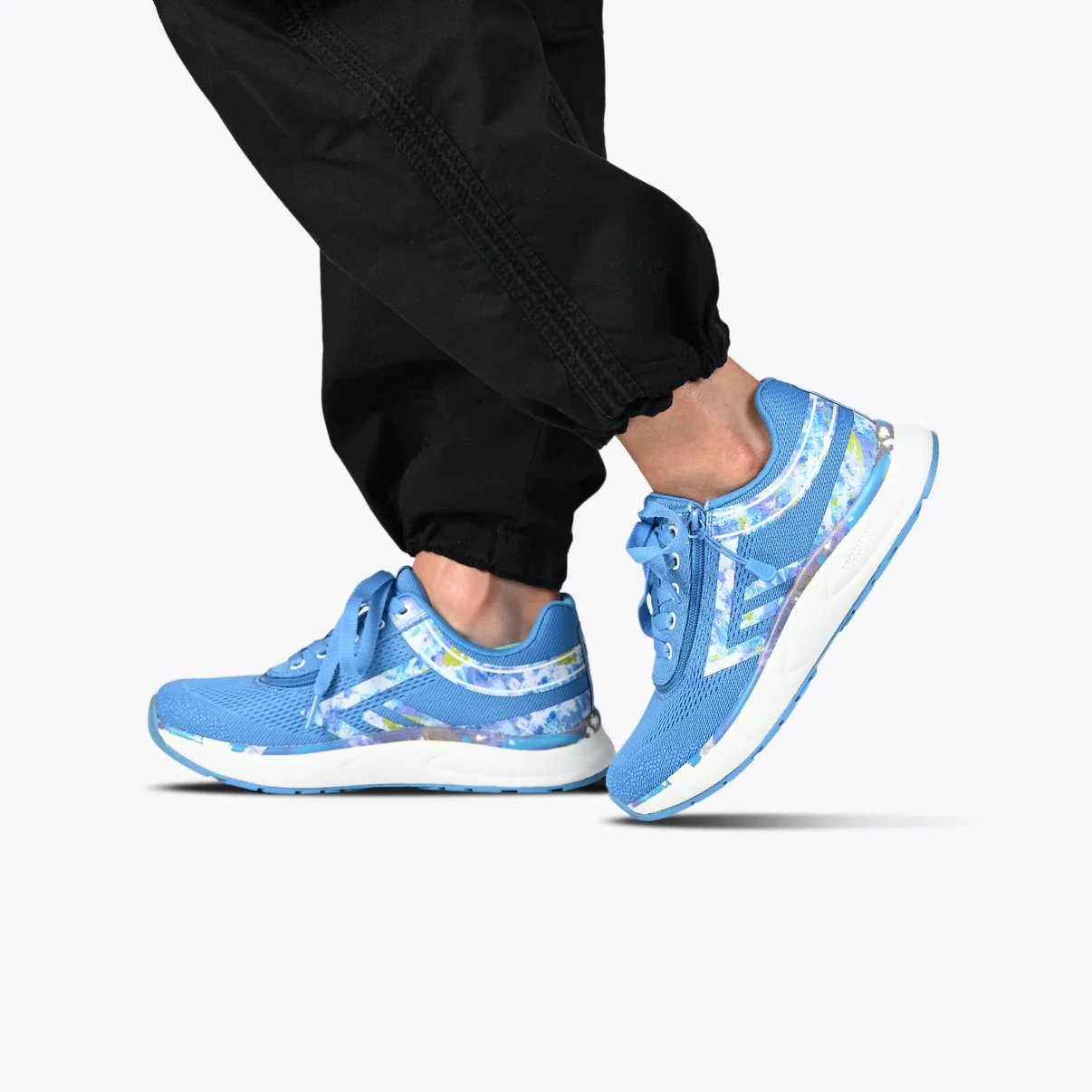 BILLY women's adaptive sneaker in a bright blue color with a marbled cool color accent pattern shown on a woman wearing black jogger pants