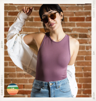 woman against a brick wall in sunglasses wearing the No Limbits Sensory Friendly tank top in a mauve pink color, with jeans and a white denim jacket