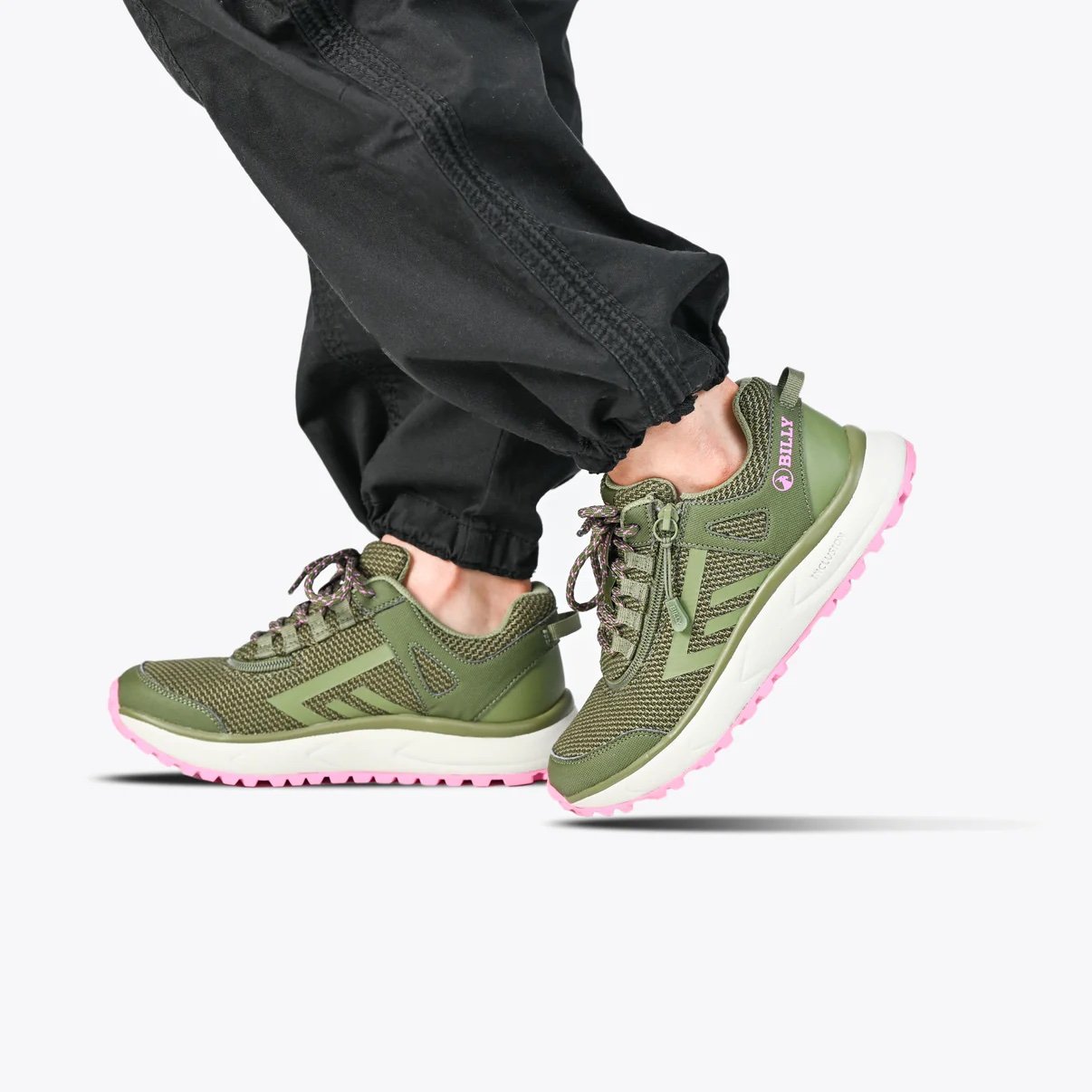 BILLY adaptive women's trail inclusion shoe in olive green with pink accents and a white rubber sole on a woman wearing black joggers
