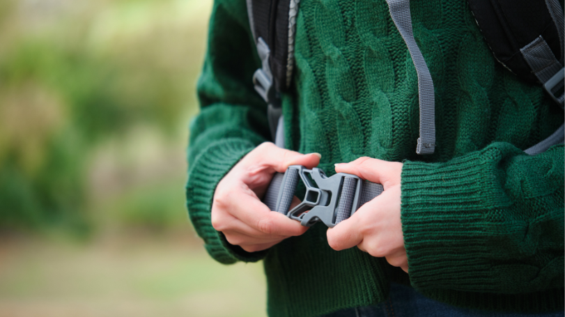 zoomed in photo of a person in a green sweater securing the hip belt of their backpack