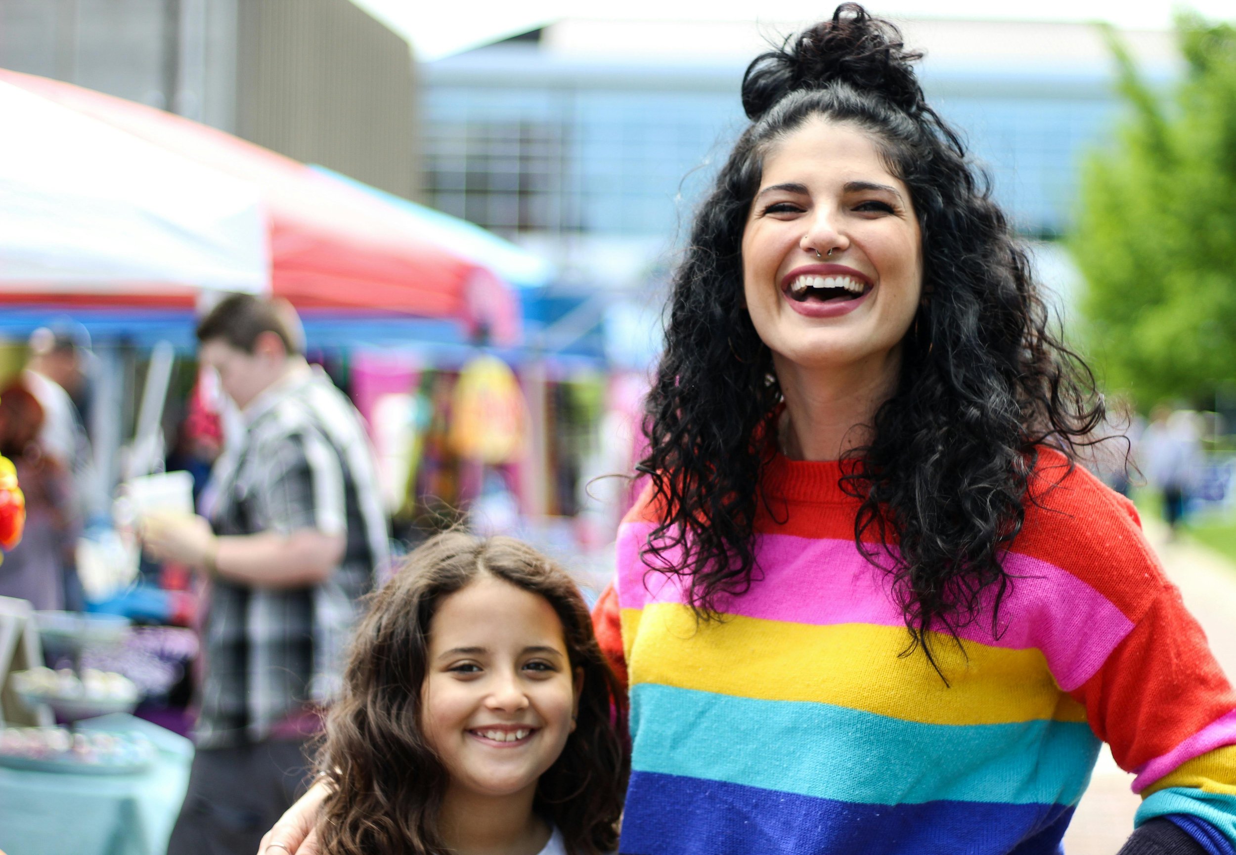 Brunette woman in rainbow sweater laughing with child.
