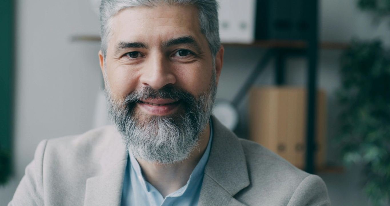 Man with a bear smiles while wearing a suit jacket.