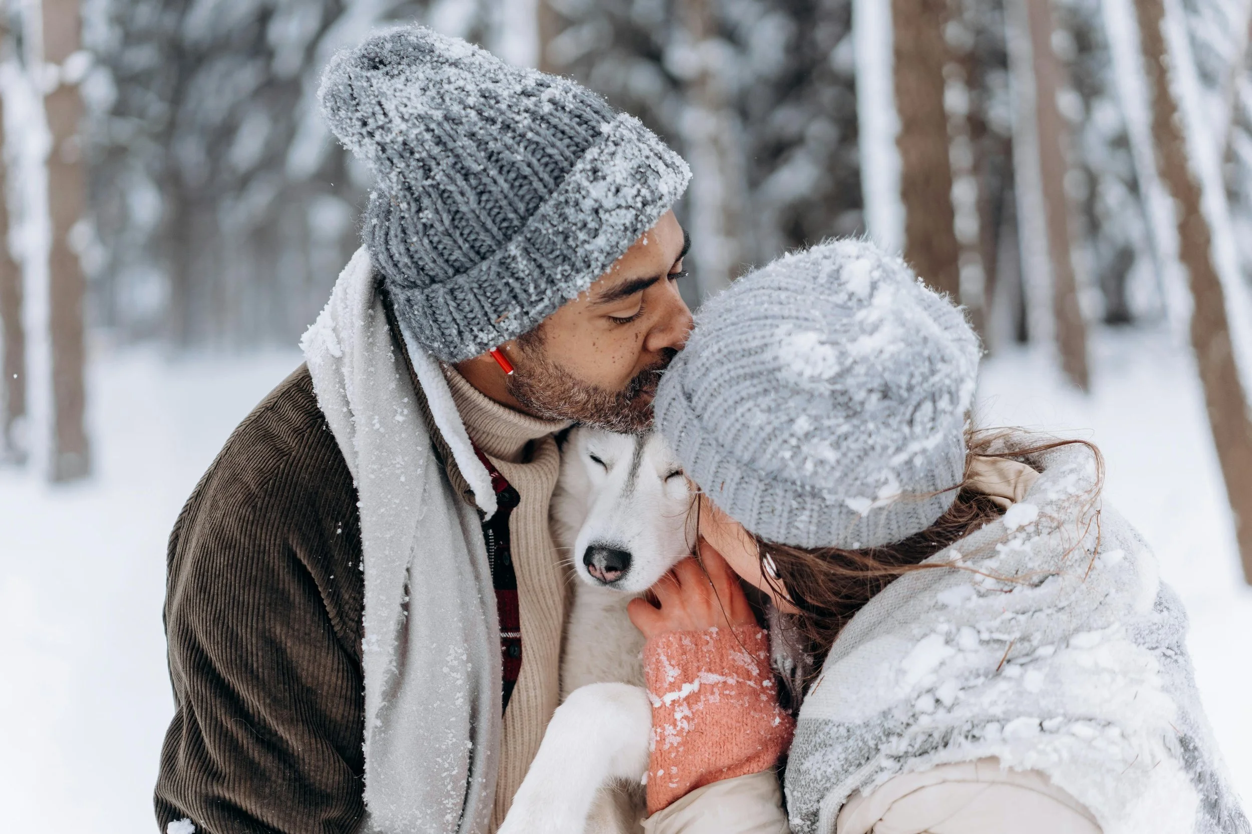Man and woman kissing dog in snow as they focus on medication management for winter.
