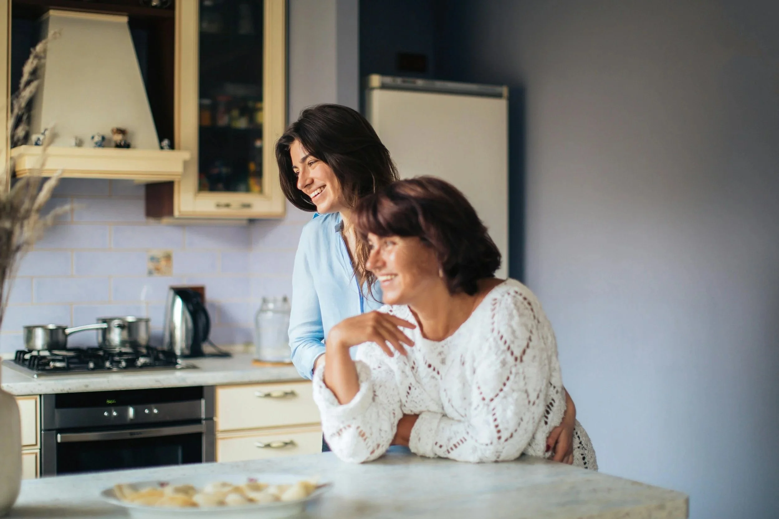 Two women laugh in a kitchen free from anxiety or depression.