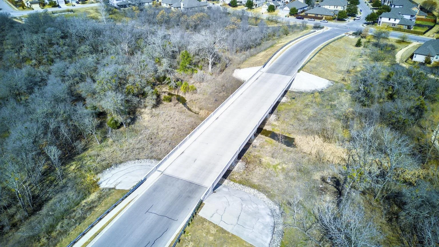 An aerial view of a bridge in a residential area with trees and houses.