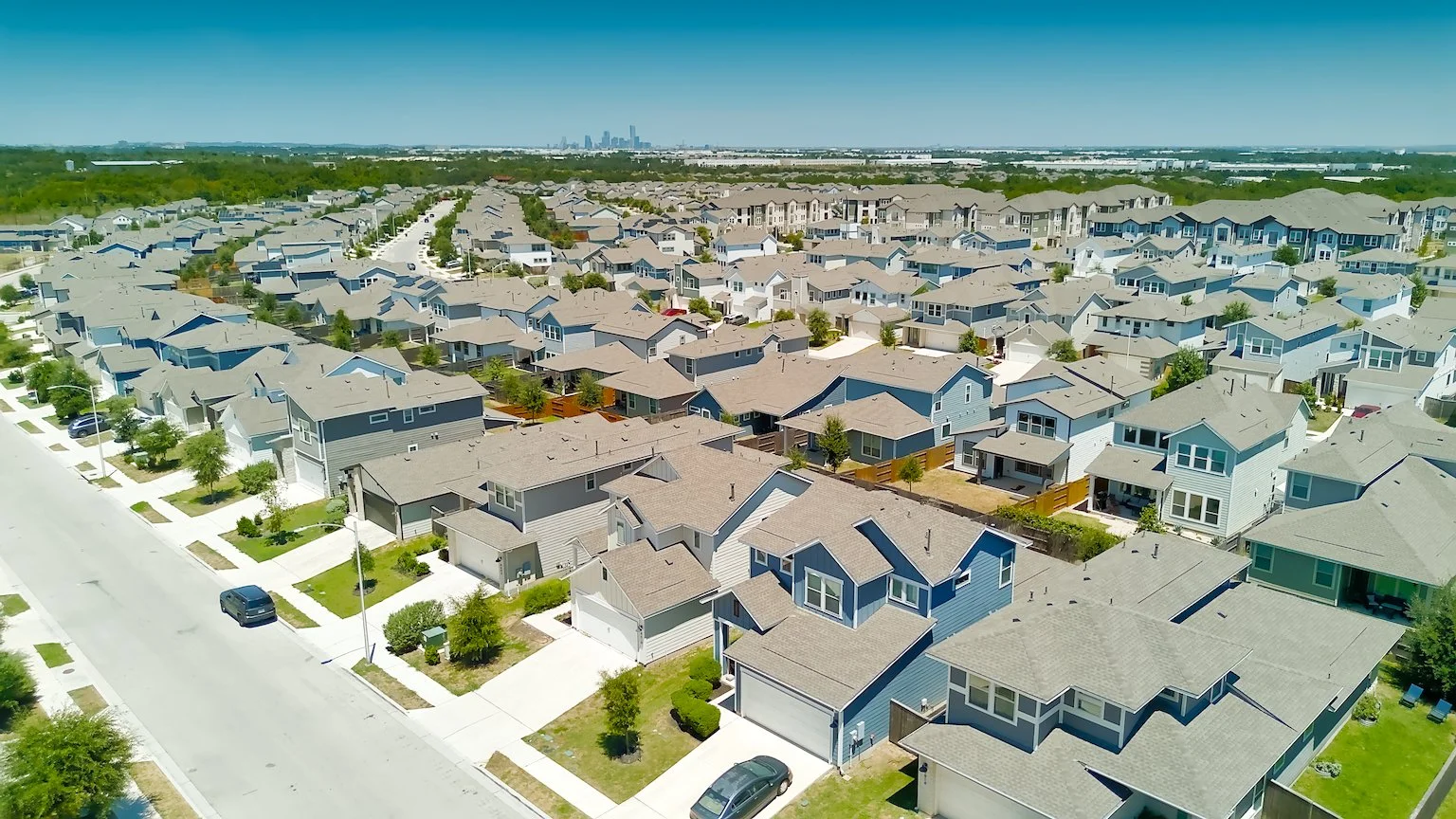 Aerial view of a suburban neighborhood with single-family homes and a city skyline in the distance.