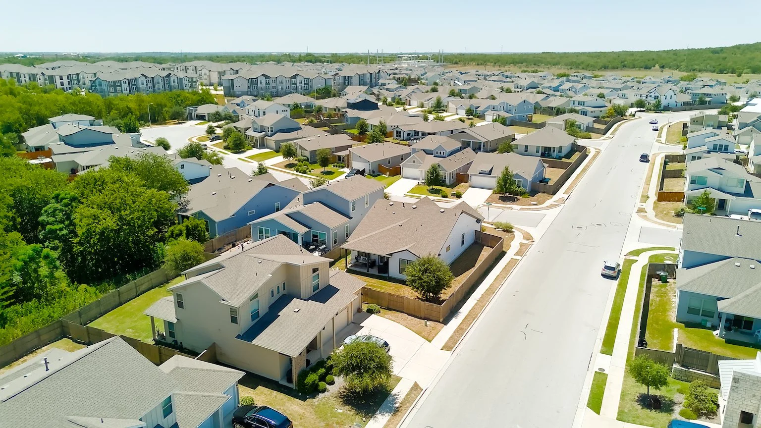 Aerial view of a suburban neighborhood with rows of houses, landscaped yards, and streets with cars parked along the curb.