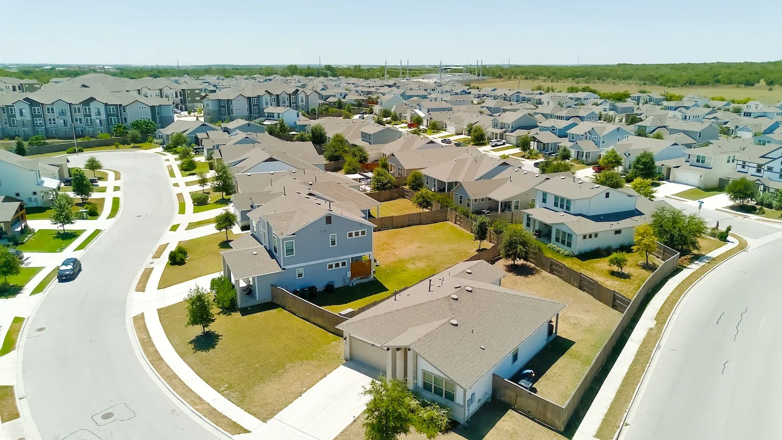 Aerial view of a new suburban neighborhood with houses, streets, trees, and open yards.