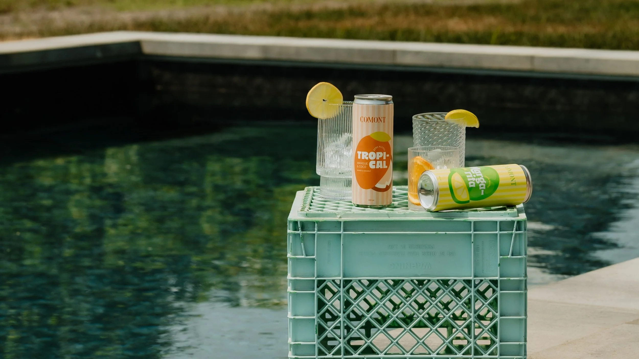 Boissons en canettes et verres avec glaçons et citrons sur une caisse près d'une piscine.