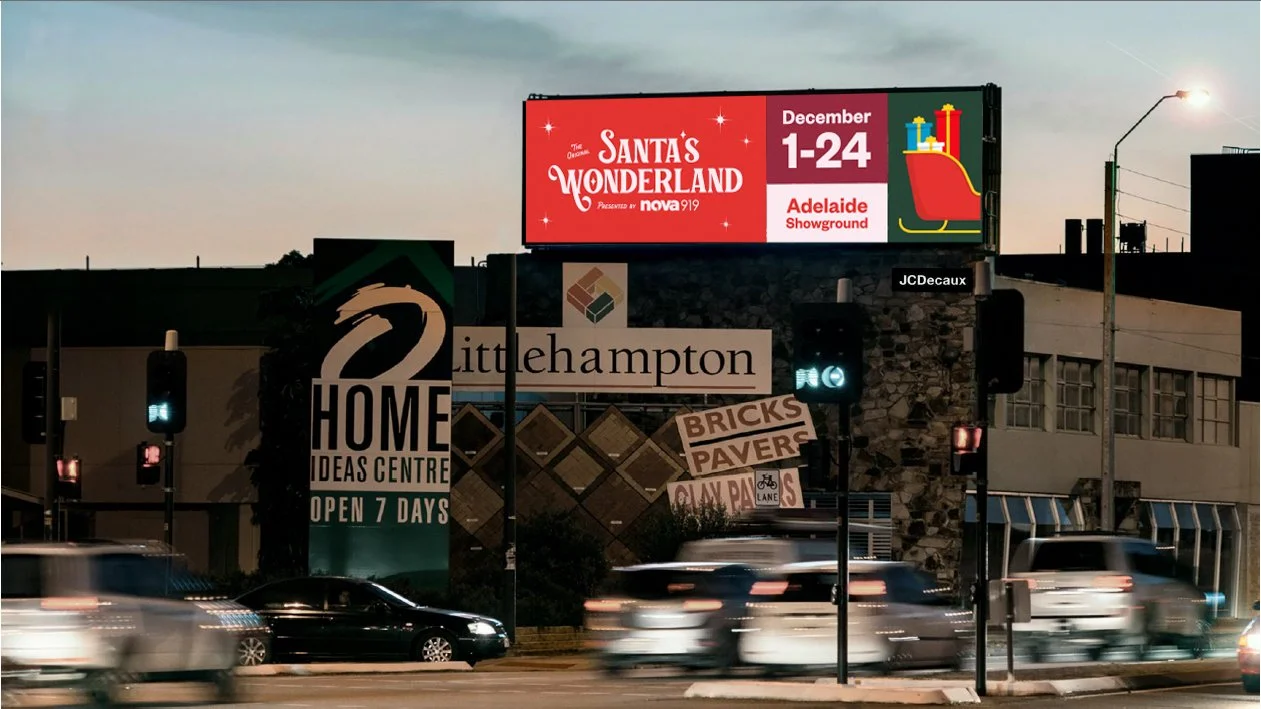 Street scene with cars and traffic lights in front of a building with a large advertisement for Littlehampton Home Ideas Centre, and a digital billboard promoting Santa's Wonderland event in Adelaide from December 1-24.