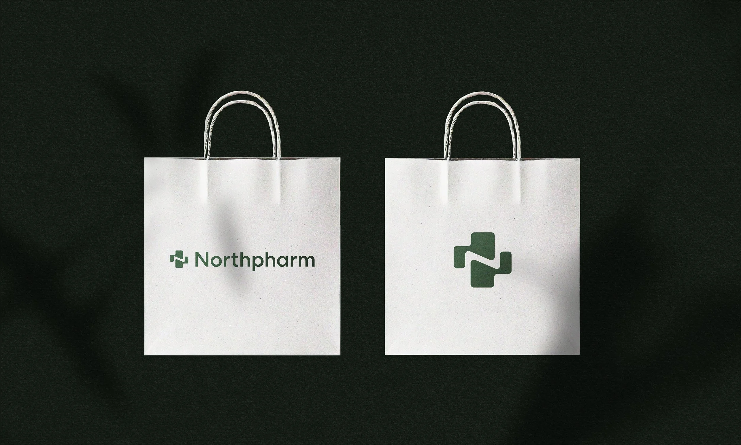 Two white shopping bags with green logos, one labeled 'Northpharm,' placed on a black surface.