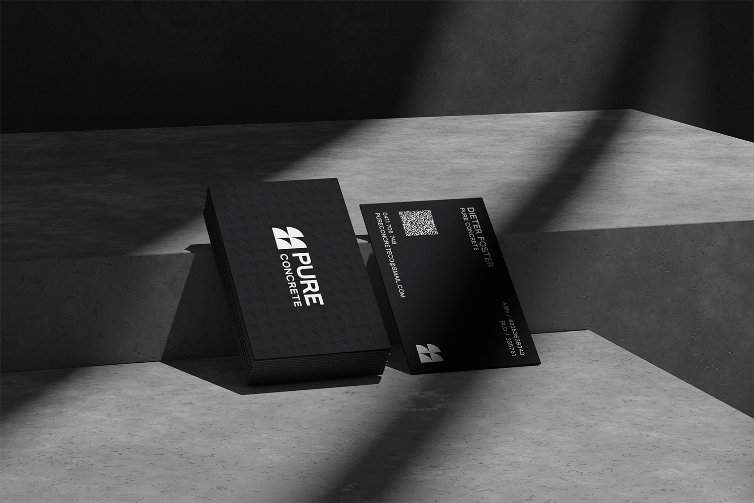 Black business card holder with business cards, one of which is leaning on the holder, displaying the logo and contact information, placed on a concrete surface with dramatic lighting and shadows.